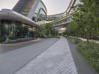 a walkway leading to buildings in an urban area with lots of glass windows and trees in front
