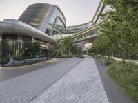 a walkway leading to buildings in an urban area with lots of glass windows and trees in front