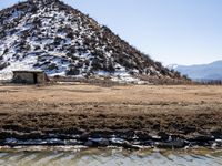 a small outhouse is standing in front of the water's edge and mountains