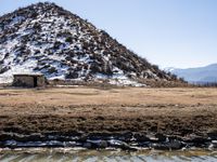 a small outhouse is standing in front of the water's edge and mountains