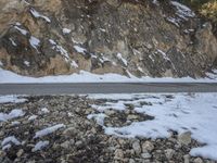 a lone car sits on a snowy mountain road by a rock formation and is approaching a steep cliff