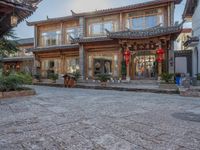 a large wooden building with chinese decorations on it and plants in front of it on a cobblestone path