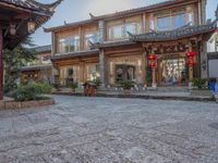 a large wooden building with chinese decorations on it and plants in front of it on a cobblestone path