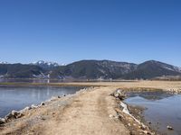 an empty dirt road is by the water with mountains in the background in this photo