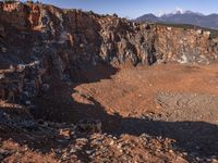 a big open pit is in the middle of mountains with snow covered mountains in the background