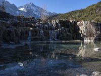 clear water flowing into the pool of an artificial pond surrounded by waterfalls and mountain ranges