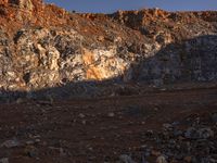 a hill with orange rocks and dirt, with a lone person walking along the sides of it