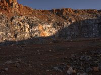 a hill with orange rocks and dirt, with a lone person walking along the sides of it