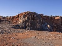 large rock formations near a dirt road and field covered with rocks and trees at the edge of rocky mountain