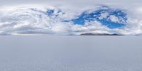 two sheep on snowy landscape in front of mountain range under cloudy sky with blue sky