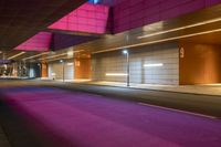 the street is lit up purple by an overhang at night time, with lights reflecting off of the wall