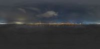 a picture taken from behind a fence looking towards a city at night, with the ocean in the foreground