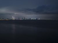 the city and its lighting are dim from a cloudy night sky over the ocean and cityscape