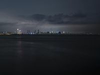 the city and its lighting are dim from a cloudy night sky over the ocean and cityscape