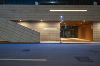 a person walking up an empty walkway next to a building at night, and lights on