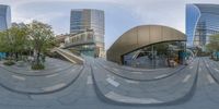 a fisheye view of some buildings and bushes in a city park with many stairs