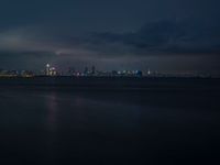 city lights shining from the sky on top of water with waves and cloudy skies in the background