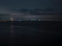 city lights shining from the sky on top of water with waves and cloudy skies in the background