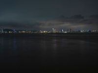 city lights shining from the sky on top of water with waves and cloudy skies in the background