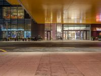 a man standing outside of a building at night with people walking in front of it