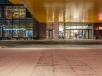 a man standing outside of a building at night with people walking in front of it