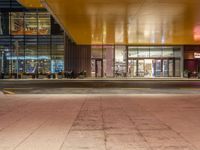 a man standing outside of a building at night with people walking in front of it