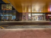 a man standing outside of a building at night with people walking in front of it