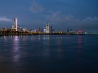 a view of the city skyline at night from across the water with clouds above it