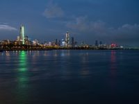 a view of the city skyline at night from across the water with clouds above it