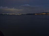 a city skyline seen from a boat at night on the water below dark clouds and light