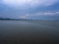 a boat on the water under clouds over a city skyline on an overcast day