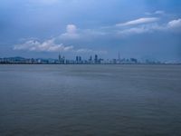 a boat on the water under clouds over a city skyline on an overcast day