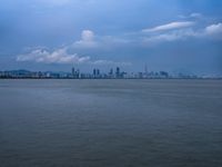 a boat on the water under clouds over a city skyline on an overcast day