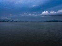 a boat on the water under clouds over a city skyline on an overcast day