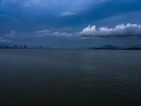 a boat on the water under clouds over a city skyline on an overcast day