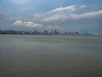 a boat on the water under clouds over a city skyline on an overcast day