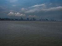 a boat on the water under clouds over a city skyline on an overcast day