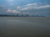 a boat on the water under clouds over a city skyline on an overcast day