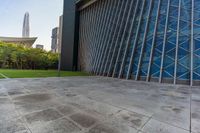 a concrete floor that is in front of tall buildings next to a green field with trees