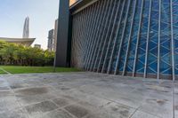 a concrete floor that is in front of tall buildings next to a green field with trees