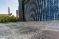 a concrete floor that is in front of tall buildings next to a green field with trees