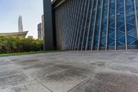 a concrete floor that is in front of tall buildings next to a green field with trees