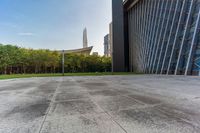 a concrete floor that is in front of tall buildings next to a green field with trees