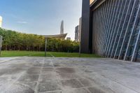 a concrete floor that is in front of tall buildings next to a green field with trees