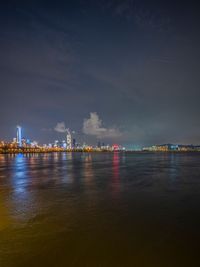 a city skyline lit up by colored lights reflecting in the water of a river at night