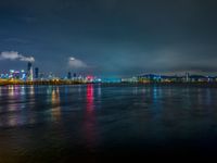 a city skyline in the distance from the water at night, all of which are lit up by colored lights