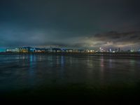 a city skyline in the distance from the water at night, all of which are lit up by colored lights