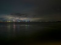 a city skyline in the distance from the water at night, all of which are lit up by colored lights