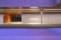 street lamps in front of building with open doors on left side of road lit by the purple lights