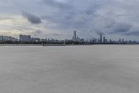 large open concrete field with city in distance and clouds above it on a sunny day